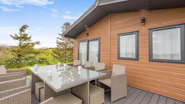 A modern outdoor patio with a glass table and wicker furniture, overlooking a green landscape. - 4 Bed in Bentham (oc-w37870) (Bentham)