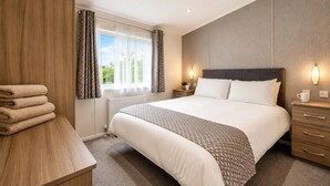 A hotel room with a large bed, bedside tables, a nightstand, a window with curtains, and a radiator. - 4 Bed in Bentham (oc-w37870) (Bentham)