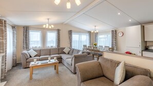 A modern living room with a sectional sofa, a dining table with chairs, and a kitchen area visible through an open door. - 4 Bed in Bentham (oc-w37870) (Bentham)