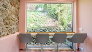 Una habitación con pared de piedra, una ventana que da a un jardín y tres sillas grises.