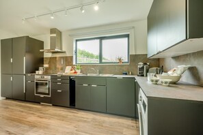 A modern kitchen with a built-in oven, a coffee maker, and a window with a view of greenery.