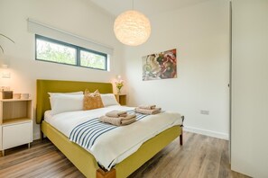 A modern hotel room with a bed, bedside table, nightstand, and a large window.