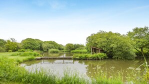 A tranquil riverside setting with a wooden structure, lush greenery, and a clear sky. - 1 Bed in St. Issey (oc-c42639) (Saint Issey)
