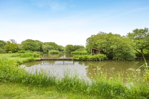 A tranquil riverside setting with a wooden structure, lush greenery, and a clear sky.