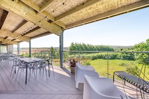 An outdoor patio with tables and chairs, a pergola, and a view of a vineyard.