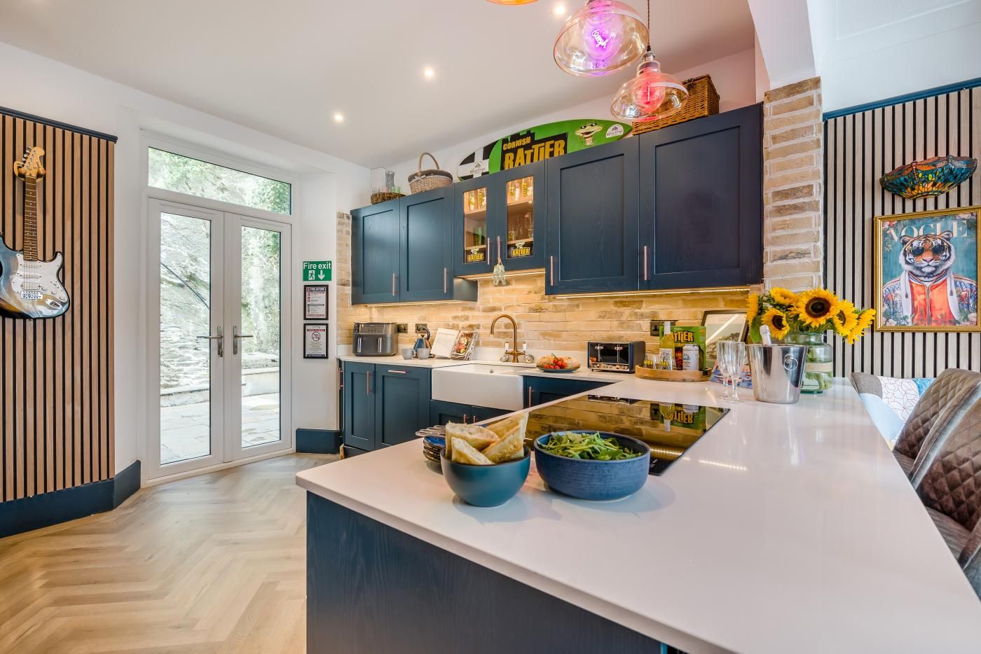 A modern kitchen with dark cabinets, a white countertop, and a fire exit sign.