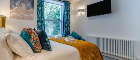 A bedroom with a bed, pillows, a window, curtains, a flat-screen TV, and a radiator.