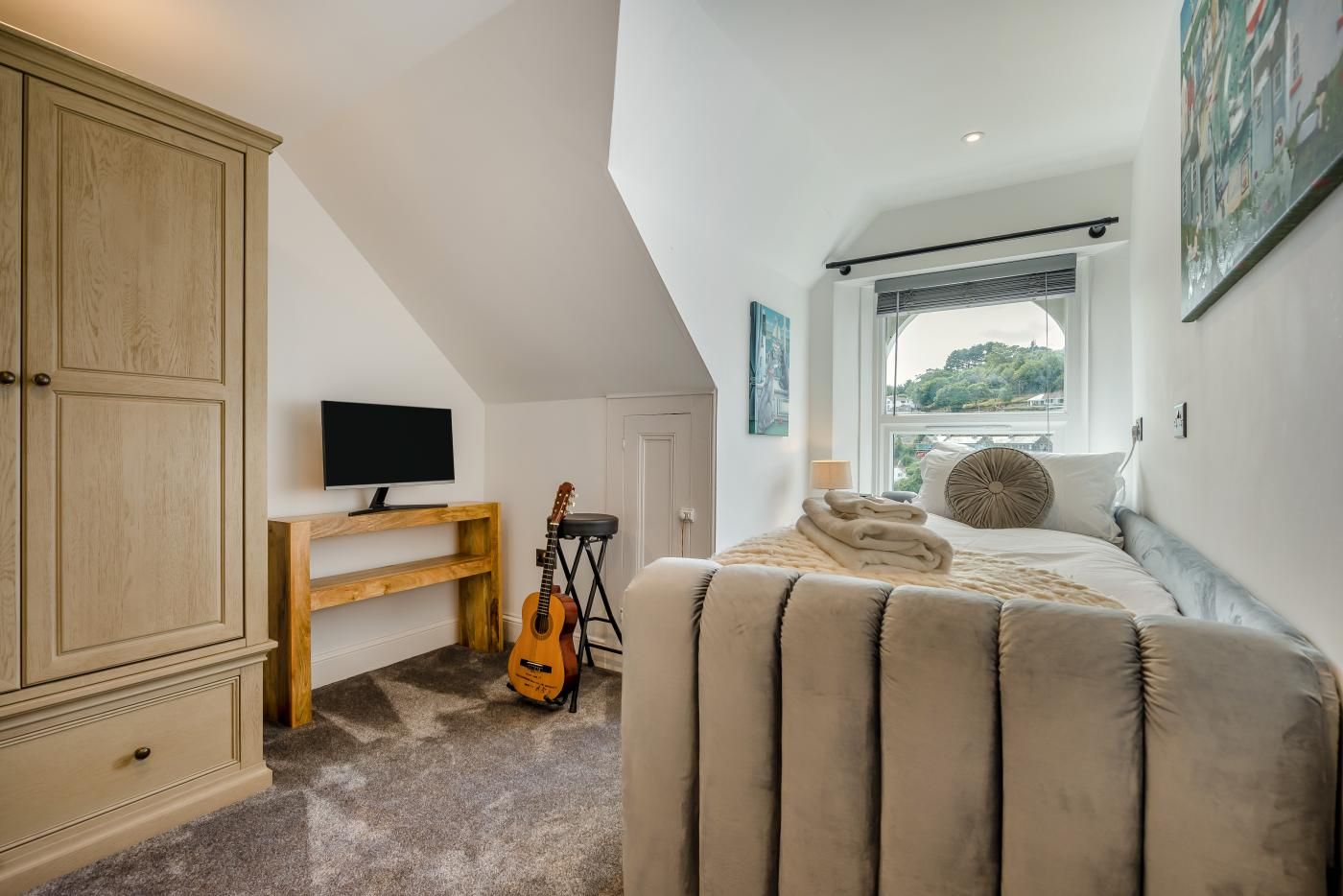 A bedroom with a bed, a desk, a guitar, and a TV.