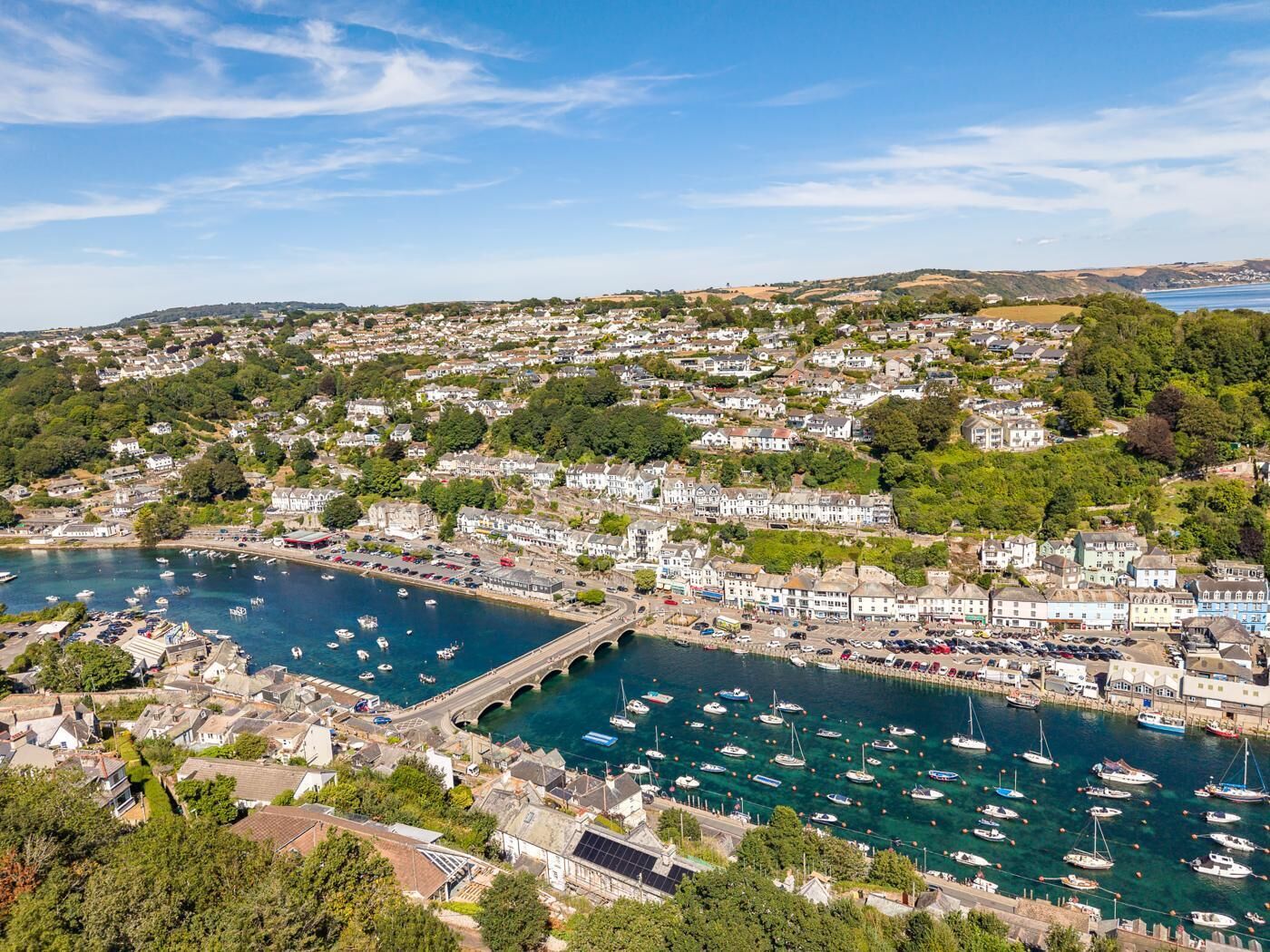 A coastal town with a marina filled with boats, surrounded by residential buildings and greenery.