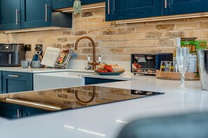 A modern kitchen with a stone backsplash, stainless steel appliances, and a central island with a sink. - 4 Bed in Looe (oc-a36906) (Looe)
