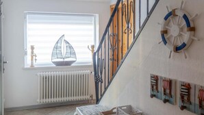 Un escalier avec une rampe, un radiateur blanc, une fenêtre avec des stores et une petite table sur laquelle se trouvent divers objets.
