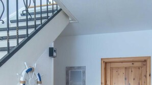 Un escalier avec une rampe, une porte en bois, un gilet de sauvetage fixé au mur, un tableau encadré et une chaise en osier avec une table.