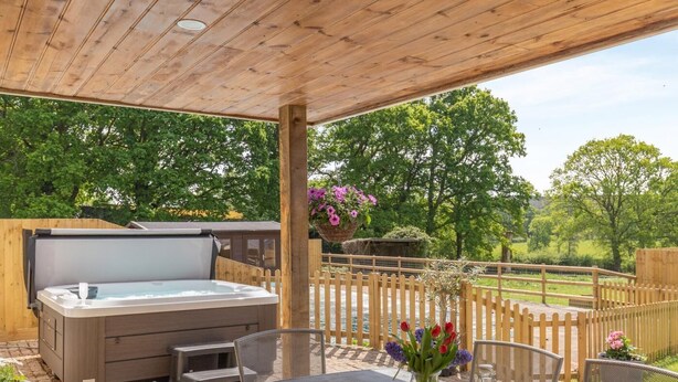 Un patio couvert avec un jacuzzi, des sièges d’extérieur et une vue sur un jardin clos.