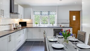 Une cuisine moderne avec des meubles blancs, un plan de travail noir et un coin repas aménagé pour six personnes, avec une table, des chaises et un vase de fleurs.