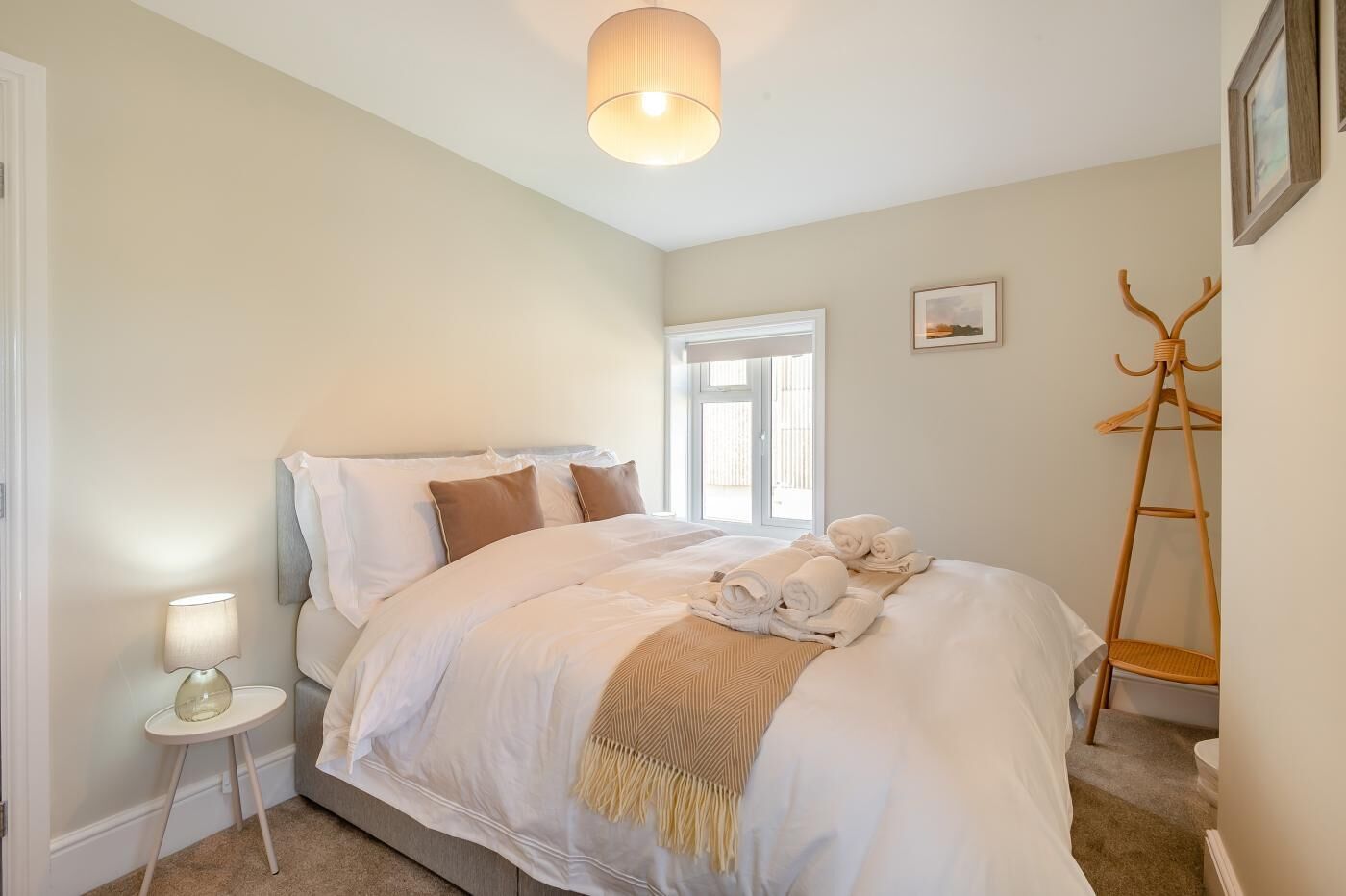 A bedroom with a bed, a bedside lamp, a window, and a coat rack.