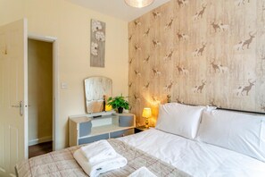A hotel room with a bed, a bedside table with a lamp, a mirror, a dresser, and a wall with a deer pattern. - 3 Bed in Reeth (oc-b42655) (Reeth)