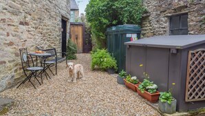 A stone building with a gravel courtyard, a wooden door, a bench, and a dog. - 3 Bed in Reeth (oc-b42655) (Reeth)