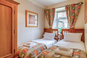 A bedroom with two beds, a wooden wardrobe, a framed picture on the wall, and a window with curtains. - 3 Bed in Reeth (oc-b42655) (Reeth)