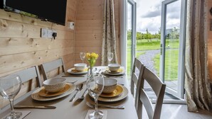 A dining table set with plates, bowls, cutlery, and glasses, with a view of a grassy area through open doors.