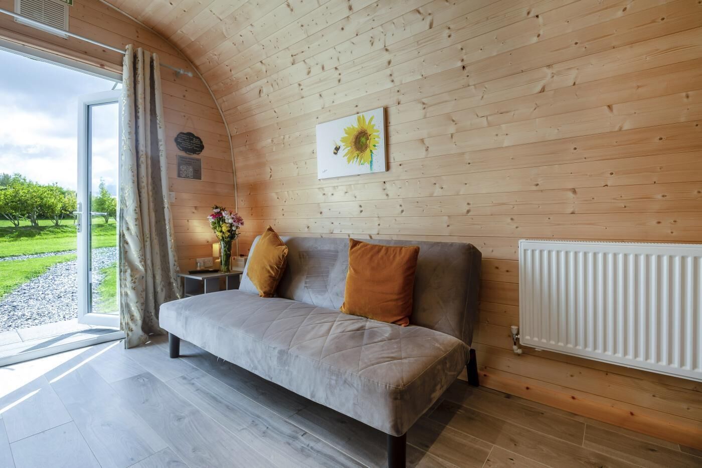 A cozy room with a sofa, a radiator, a window with curtains, and a sunflower painting on the wall.