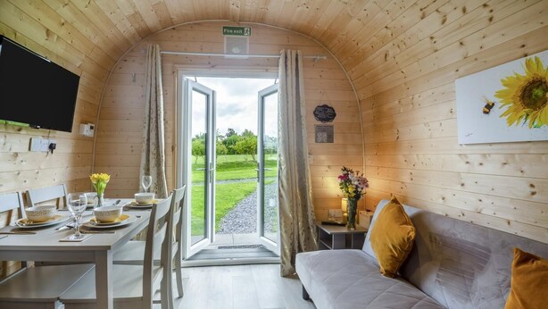 A cozy cabin interior with a dining area, a sofa, and a door leading outside.