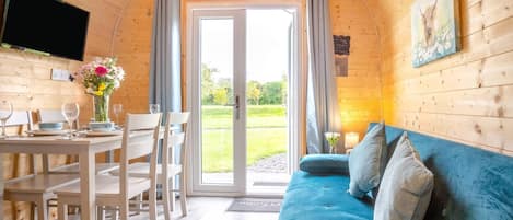 Interior acogedor de una cabaña con zona de comedor, sofá y señal de salida de incendios.