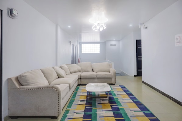 A modern living room with a beige sectional sofa, a glass coffee table, and a colorful geometric rug.