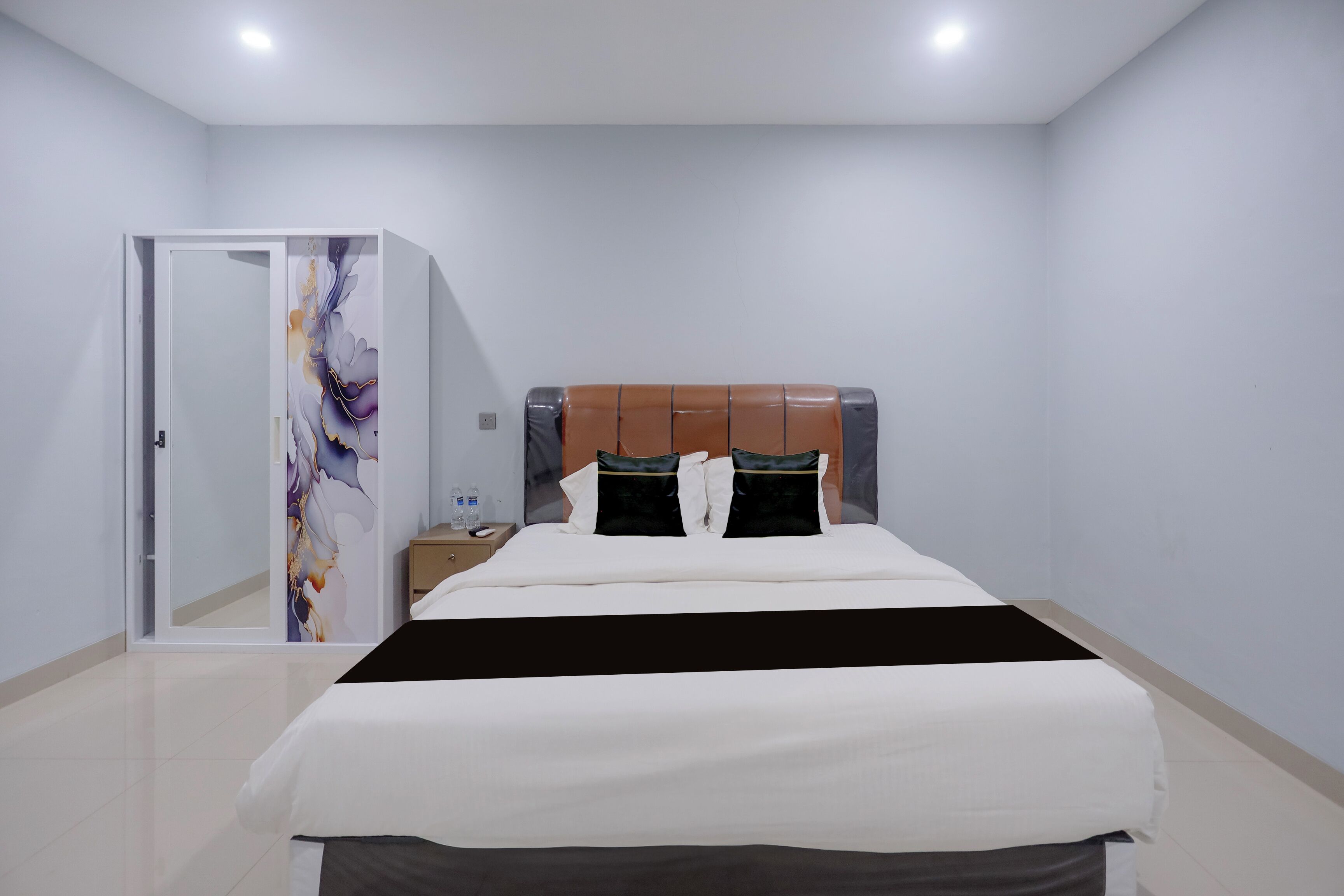 A hotel room with a bed, a nightstand, a mirror, and a door.
