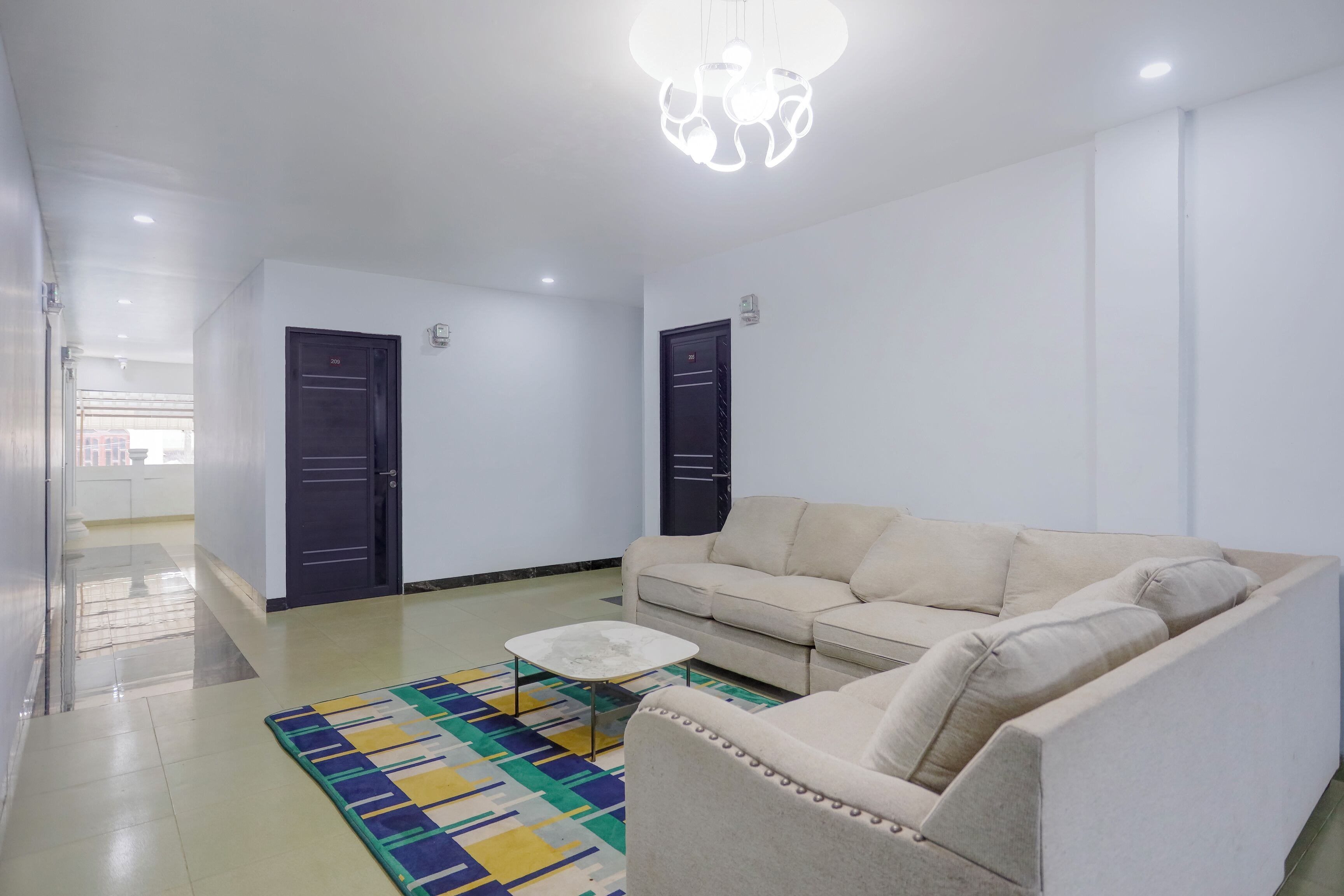 Sala de estar con un sofá, una mesa de centro y una alfombra estampada. Hay dos puertas y una lámpara en el techo.