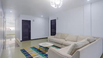 Sala de estar con un sofá, una mesa de centro y una alfombra estampada. Hay dos puertas y una lámpara en el techo.