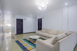 A living room with a sofa, a coffee table, and a patterned rug. There are two doors and a ceiling light fixture.