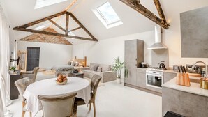A spacious living area with a high ceiling, exposed wooden beams, a dining table with chairs, a sofa, and a kitchen area with modern appliances. - 1 Bed in Gembling (oc-s42456) (Gembling)