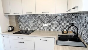 A kitchen with white cabinets, a black and white patterned backsplash, a black stove, and a sink with a black faucet. - Large Apartment in Dziwnowek, Close to the sea (Dziwnów)