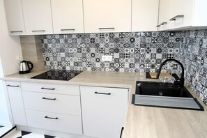 A kitchen with white cabinets, a black and white patterned backsplash, a black stove, and a sink with a black faucet. - Large Apartment in Dziwnowek, Close to the sea (Dziwnów)