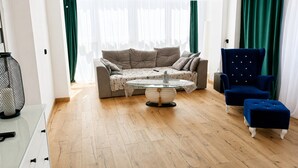 A living room with a sofa, a round coffee table, a blue armchair, and a green curtain. - Large Apartment in Dziwnowek, Close to the sea (Dziwnów)