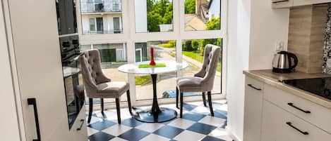 Une cuisine moderne avec un sol à carreaux noirs et blancs, deux chaises, une table ronde et une vue sur un quartier résidentiel grâce à de grandes fenêtres.