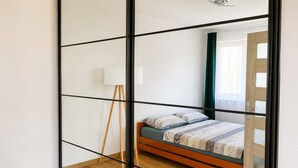 A bedroom with a wooden floor, a bed with patterned bedding, a bedside lamp, and a large mirror. - Large Apartment in Dziwnowek, Close to the sea (Dziwnów)
