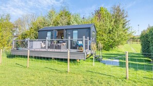 Ein modernes, eingeschossiges Haus mit einer Terrasse, umgeben von einem eingezäunten Garten und Bäumen.
