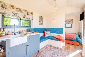 A compact kitchen with a sink, toaster, and breakfast items, a blue sofa with cushions, and a bed with a red blanket. - 1 Bed in Newall With Clifton (oc-t42700) (Newall With Clifton)