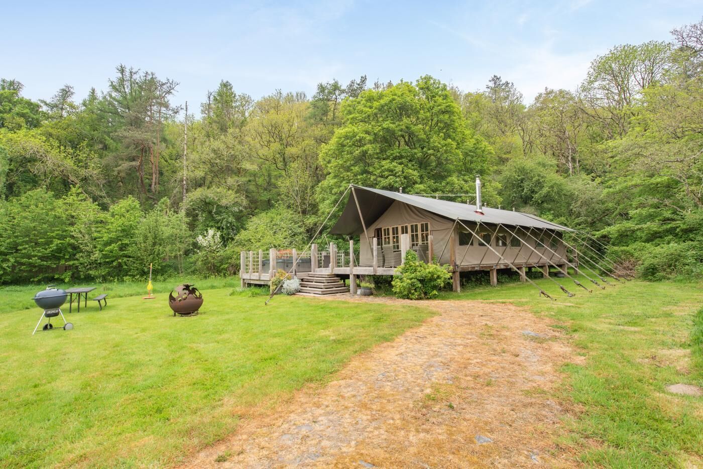 A rustic cabin with a porch, a grill, and a pot on the grass.