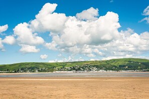 A coastal landscape with a sandy beach, a town in the background, and rolling green hills. - 4 Bed in Cwmllinau (oc-d42709) (Cwm-Llinau)