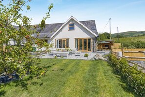 Ein Haus mit geneigtem Dach, einer Steinterrasse und einer Holzterrasse.
