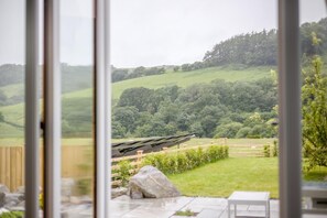 A view through a glass door of a patio area with a wooden fence, a rock, and a white table. - 4 Bed in Cwmllinau (oc-d42709) (Cwm-Llinau)
