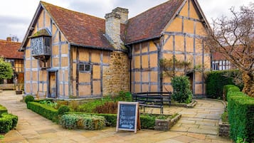 A traditional half-timbered building with a stone chimney, a signboard, and a stone pathway leading to a bench.