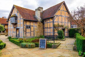 A traditional half-timbered building with a stone chimney, a signboard, and a stone pathway leading to a bench.