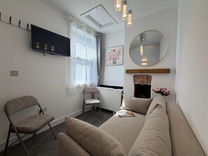 A modern bedroom with a sofa, a chair, a flat-screen TV, a fireplace, and a mirror.