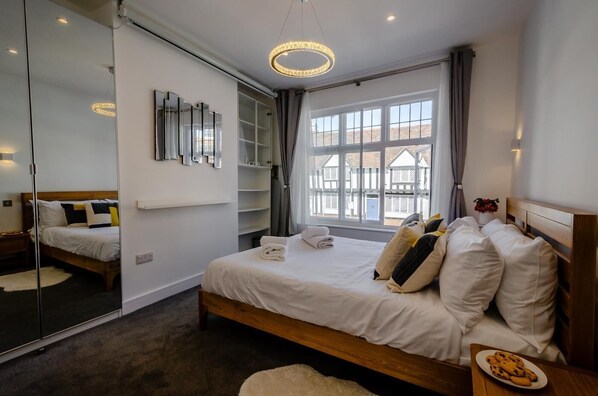 A bedroom with a large bed, bedside tables, a mirror, a window with curtains, and a view of the outside.