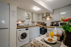 A modern kitchen with a washing machine, oven, microwave, and a dining area with a table set for two.