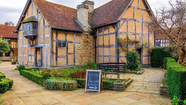 A traditional half-timbered building with a stone chimney, a signboard, and a stone pathway leading to a bench. - 2 Bed in Warwick (oc-c41051) (Warwick)