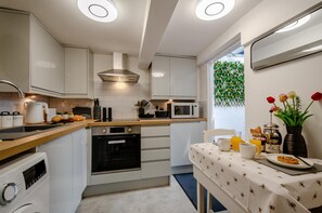 A modern kitchen with white cabinetry, a built-in oven, a microwave, and a dining area with a table set for breakfast.